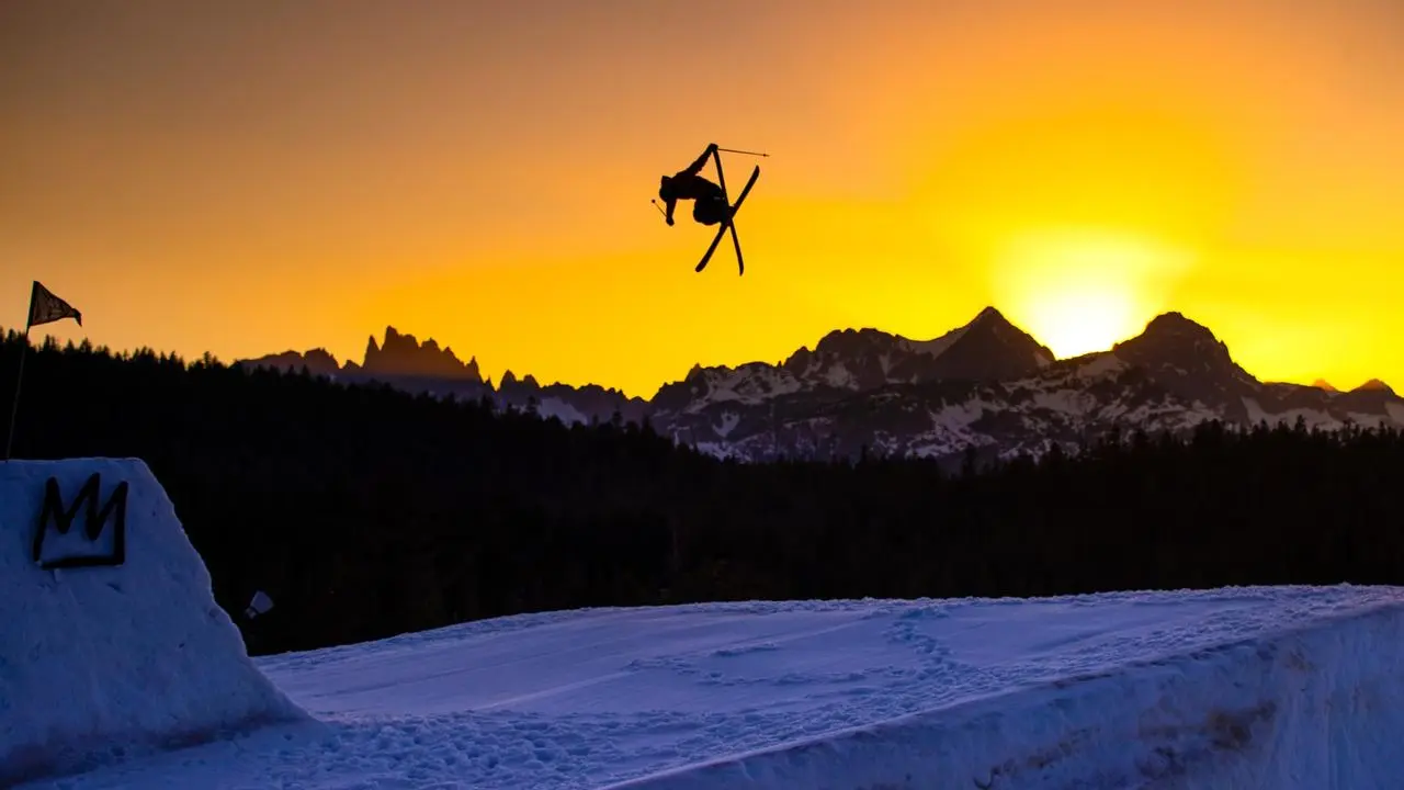 A skier doing a trick off a ski jump at sunset
