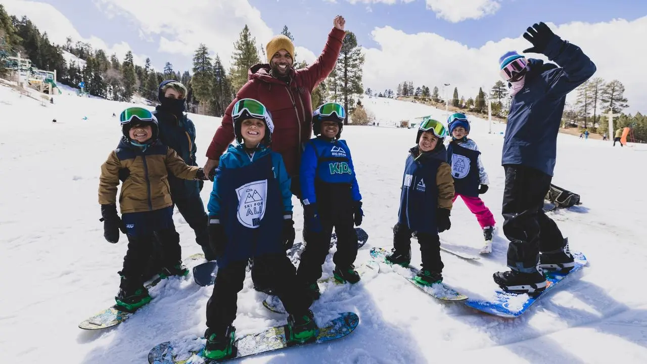 Two adults with a group of kids wearing snowboards, everyone is smiling at the camera
