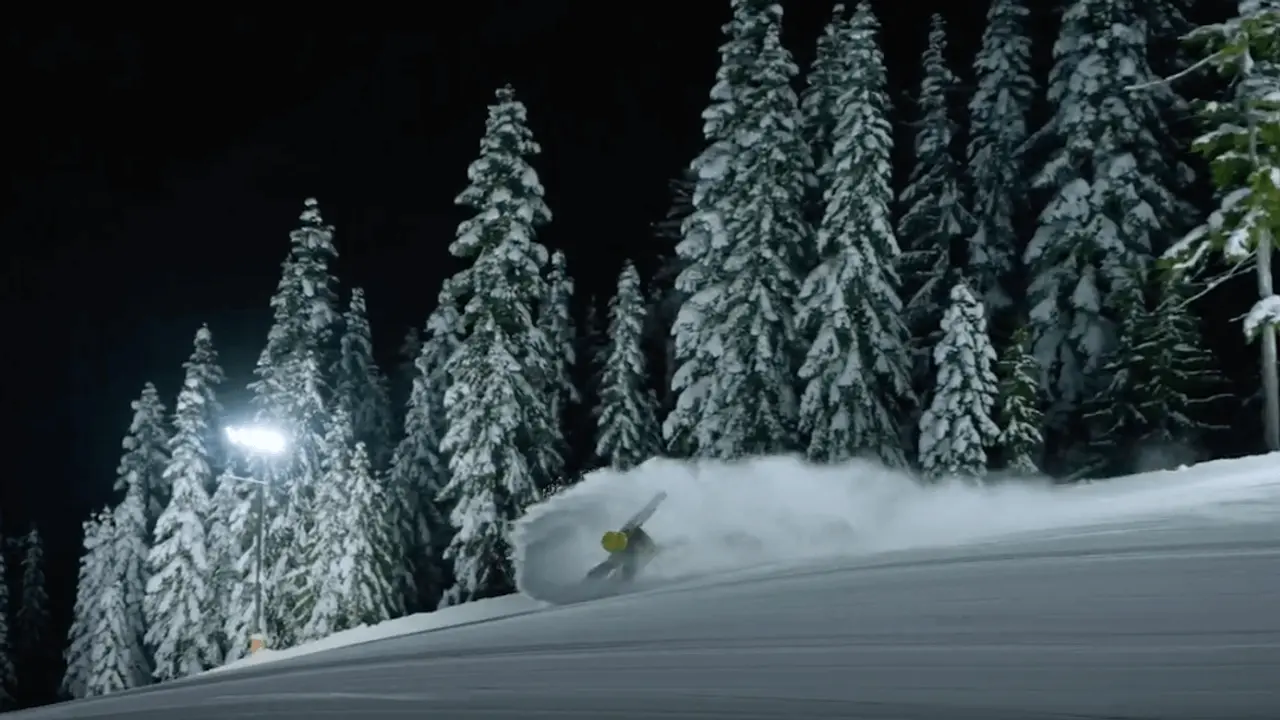 Person snowboarding down a snowy trail at night with lights shining on the run