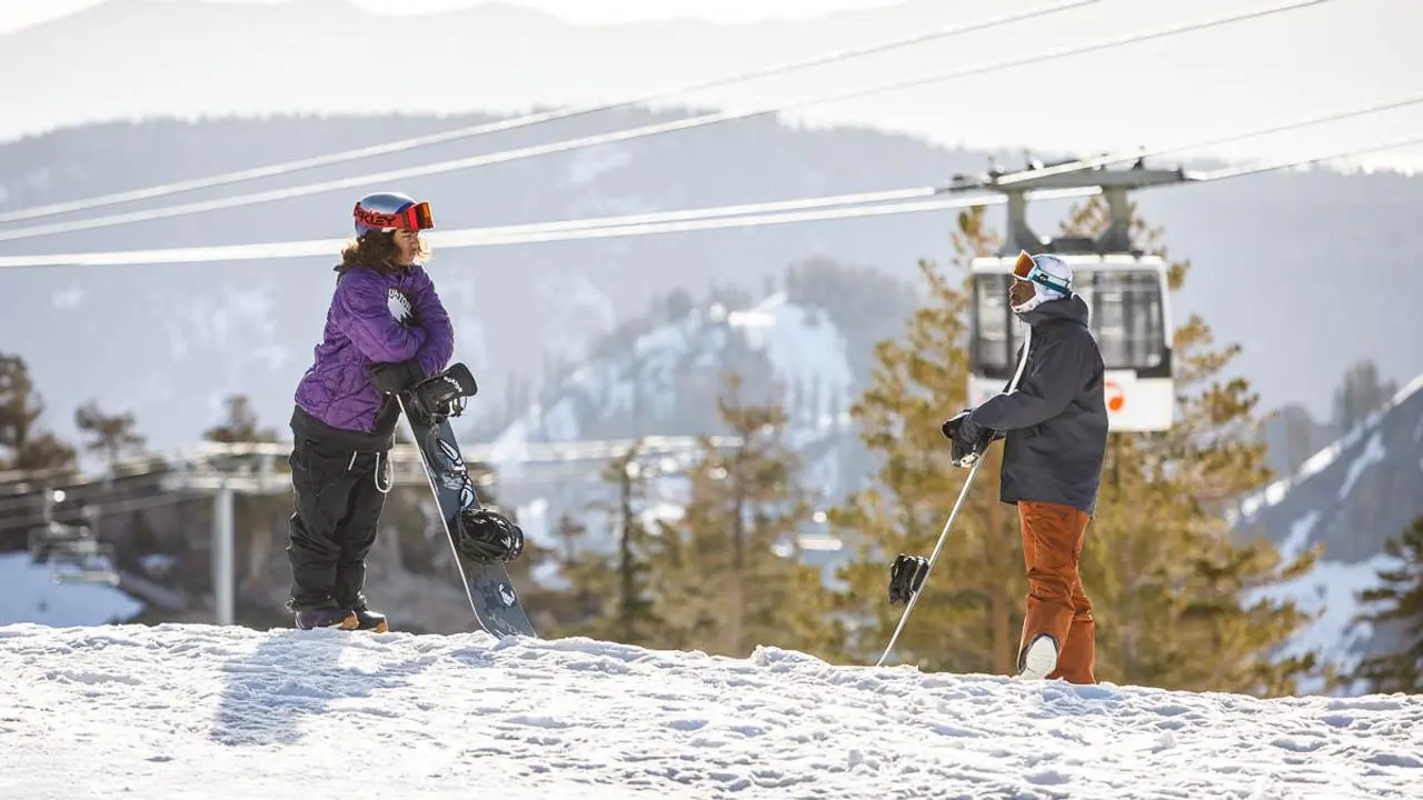 Two people in winter gear holding snowboards