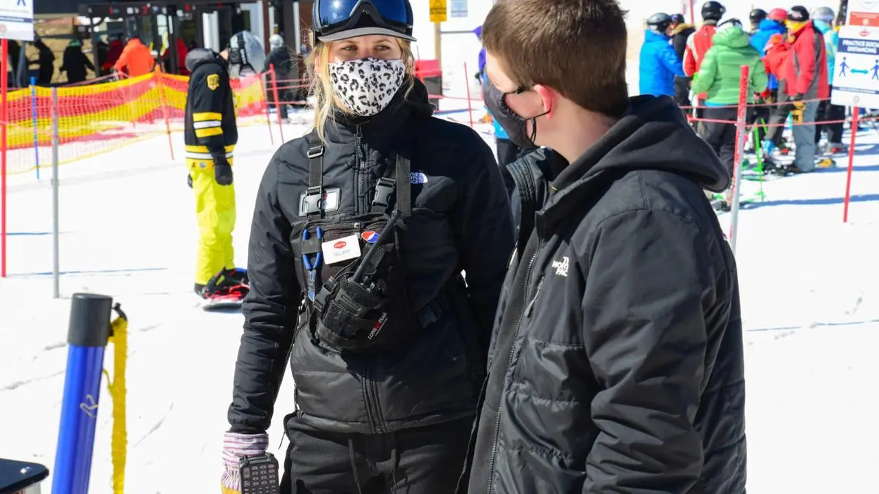 Two adults in winter gear wearing face masks talking to each other