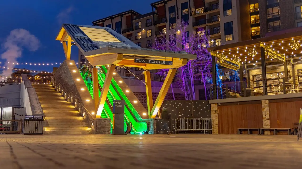 An escalator lit up at night as it leads into the base area of a ski resort