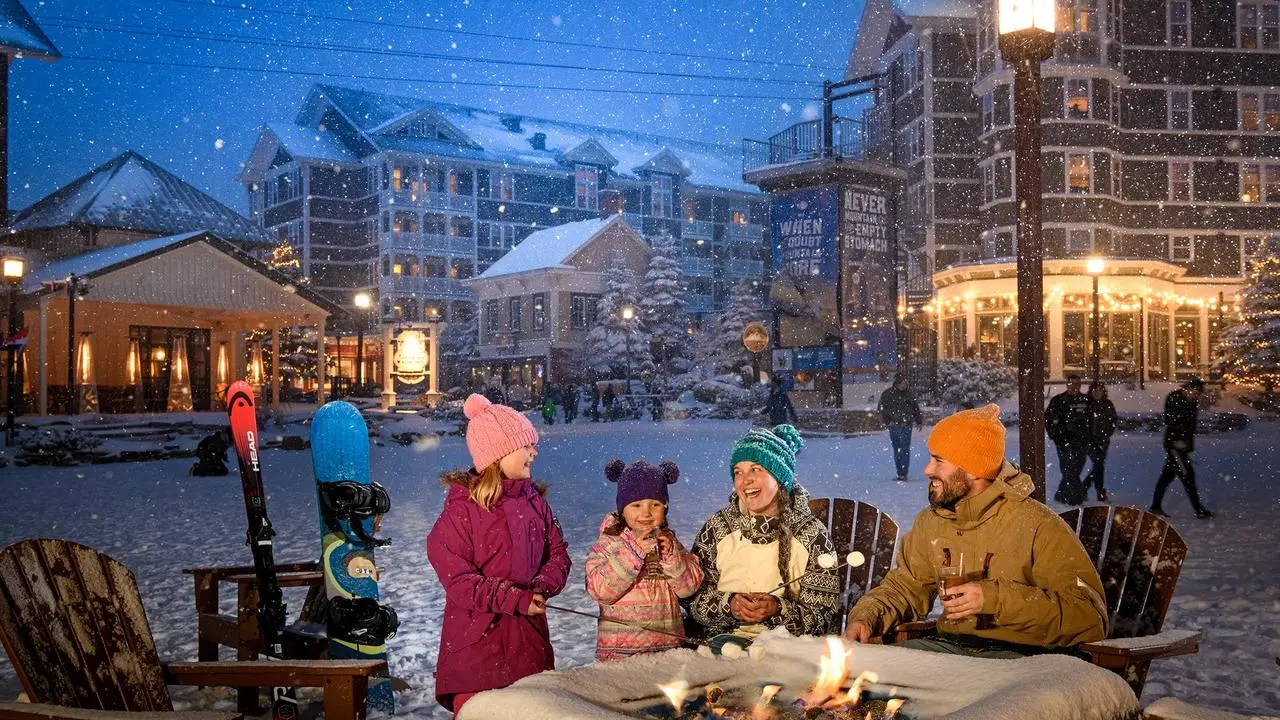 A family roasting marshmallows around a fire pit as snow falls