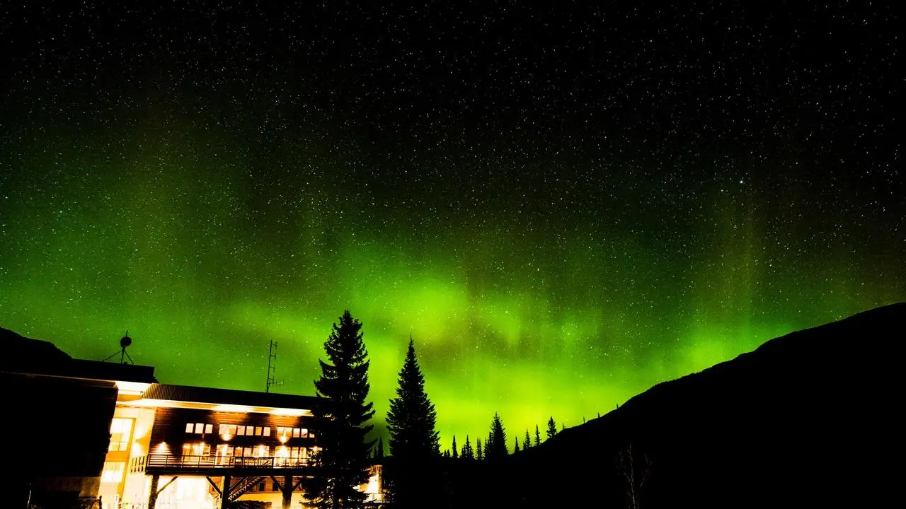 A mountain lodge illuminated at night with the northern lights shining in the sky