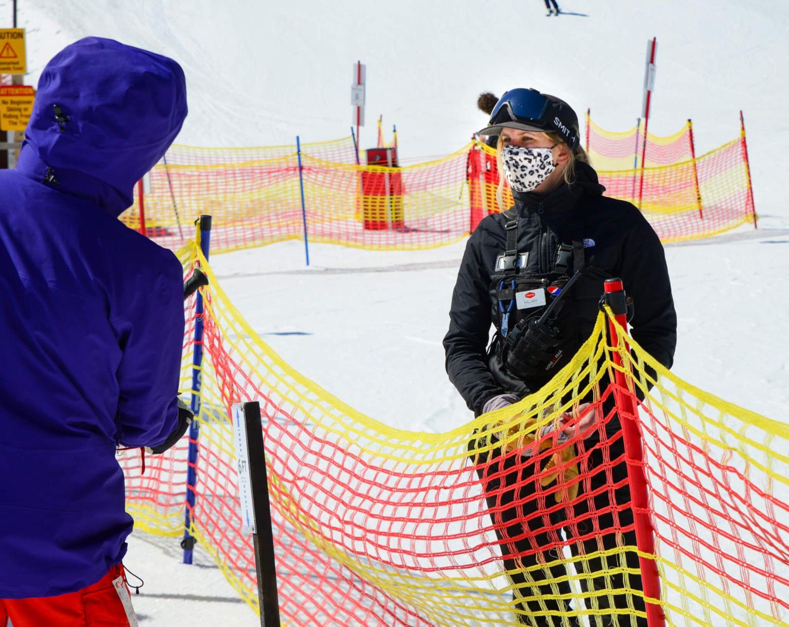 Adult in winter gear talking to a customer at a ski resort