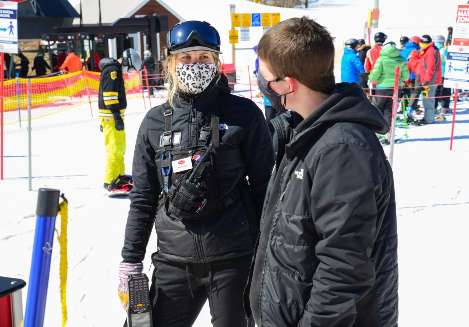 Two adults in winter gear wearing face masks talking to each other
